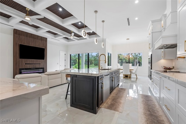 kitchen with ceiling fan, white cabinets, sink, a kitchen island with sink, and a large fireplace