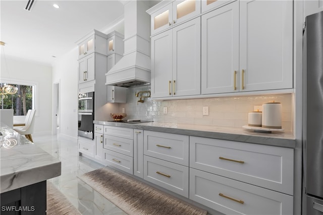 kitchen featuring appliances with stainless steel finishes, white cabinets, backsplash, light stone countertops, and custom exhaust hood