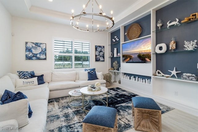 living room with wood-type flooring, ornamental molding, a tray ceiling, and an inviting chandelier