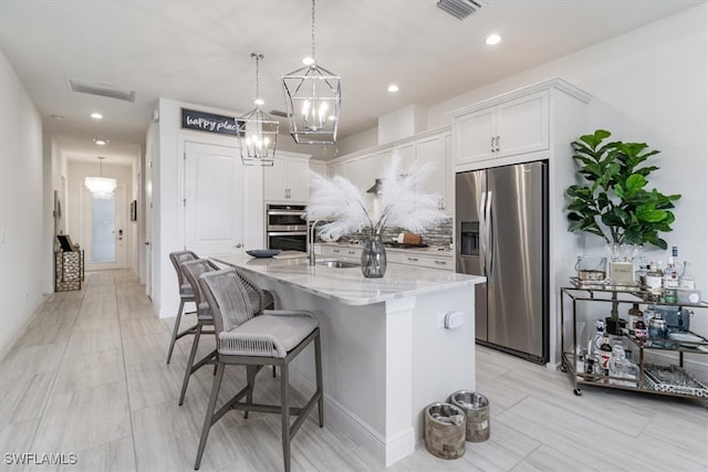 kitchen with light stone countertops, a kitchen bar, a kitchen island with sink, white cabinets, and appliances with stainless steel finishes