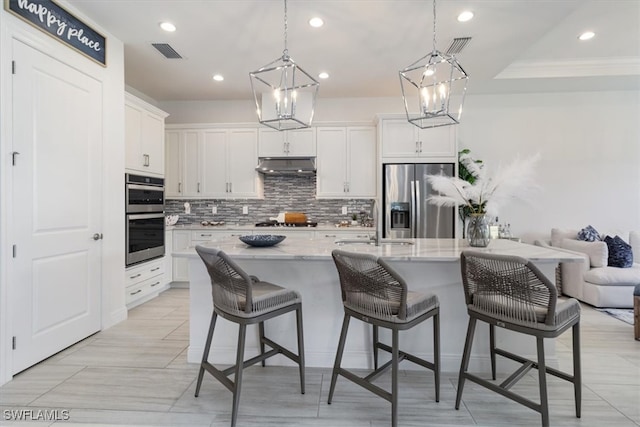 kitchen with a kitchen bar, tasteful backsplash, stainless steel appliances, white cabinetry, and hanging light fixtures