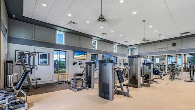 exercise room featuring ceiling fan, light colored carpet, and a towering ceiling