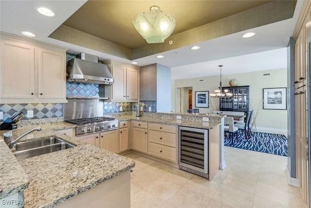 kitchen with sink, stainless steel gas cooktop, kitchen peninsula, wall chimney exhaust hood, and wine cooler