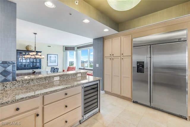 kitchen with light brown cabinetry, light stone counters, built in fridge, hanging light fixtures, and wine cooler