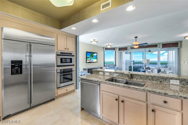 kitchen with sink, light stone countertops, light brown cabinetry, appliances with stainless steel finishes, and ceiling fan