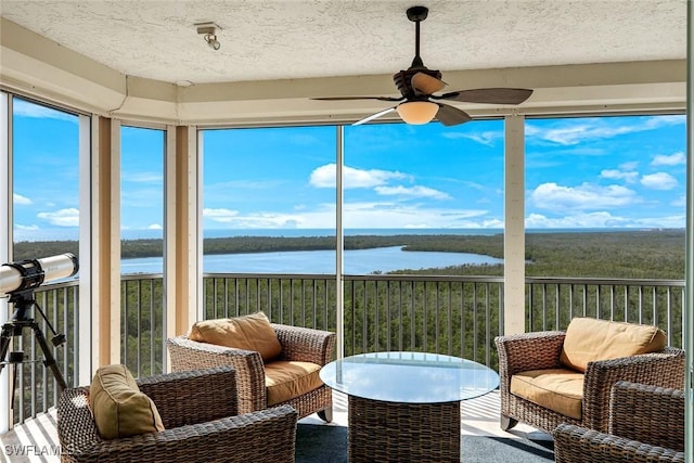 sunroom / solarium featuring ceiling fan, a water view, a textured ceiling, and carpet floors