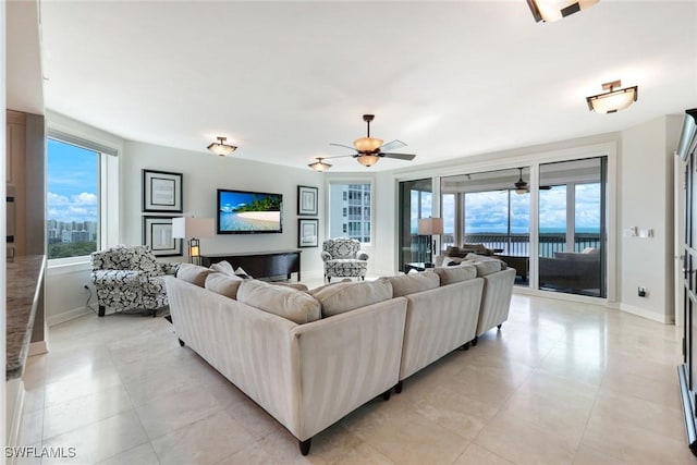 living area featuring light tile patterned flooring, plenty of natural light, a ceiling fan, and baseboards