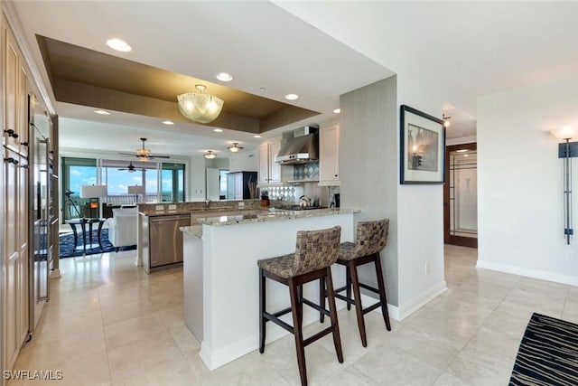 kitchen with recessed lighting, wall chimney exhaust hood, a peninsula, baseboards, and dishwasher