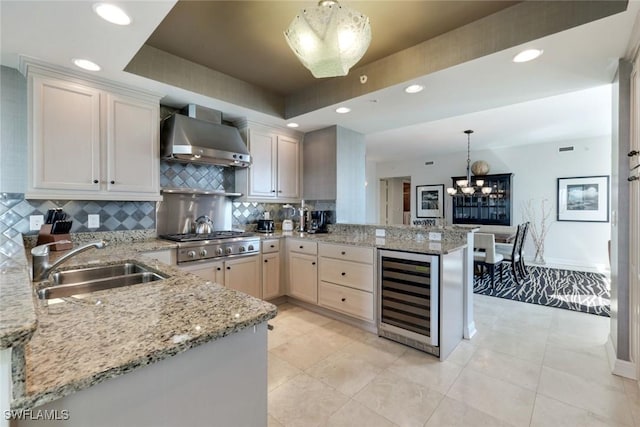 kitchen featuring stainless steel gas cooktop, a sink, a peninsula, wall chimney range hood, and beverage cooler