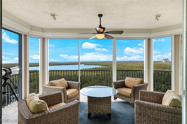 sunroom / solarium with a ceiling fan, a water view, and a textured ceiling