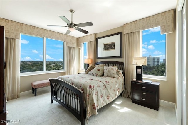 bedroom with a ceiling fan, multiple windows, light colored carpet, and baseboards