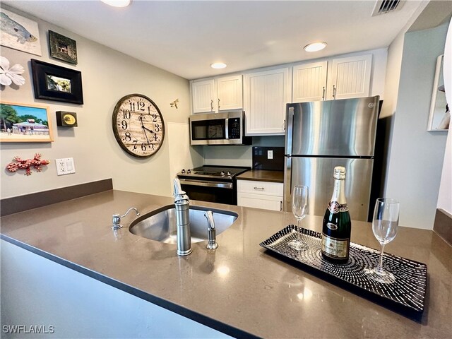 kitchen featuring sink, appliances with stainless steel finishes, kitchen peninsula, and white cabinetry