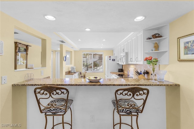 kitchen featuring a breakfast bar area, light stone counters, kitchen peninsula, and white cabinets