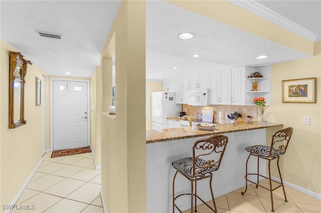 kitchen with white cabinets, backsplash, light stone countertops, white appliances, and kitchen peninsula