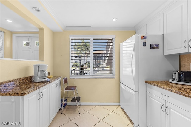 kitchen with white cabinets, dark stone countertops, light tile patterned floors, crown molding, and white fridge