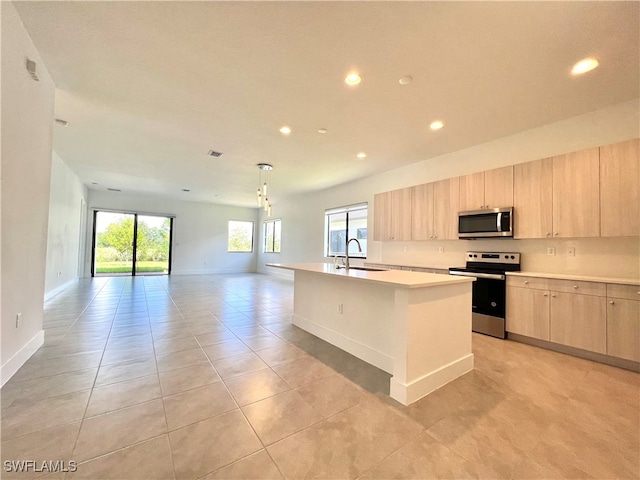 kitchen with appliances with stainless steel finishes, a wealth of natural light, sink, and a center island with sink