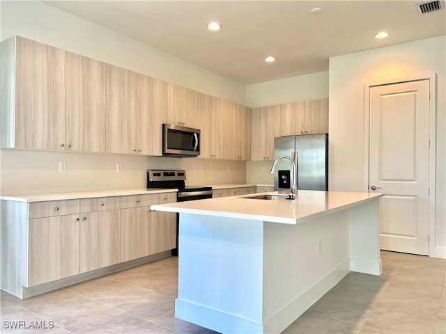 kitchen with appliances with stainless steel finishes, a kitchen island with sink, and light brown cabinetry