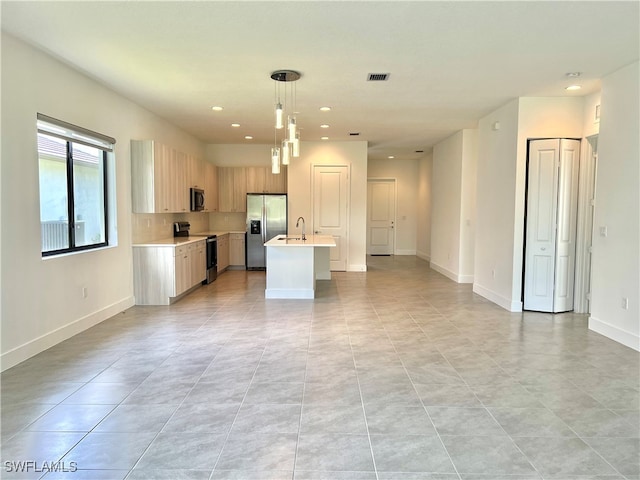 kitchen with hanging light fixtures, light tile patterned floors, appliances with stainless steel finishes, sink, and an island with sink