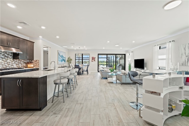 kitchen with tasteful backsplash, dark brown cabinets, light hardwood / wood-style flooring, a kitchen breakfast bar, and stainless steel gas stovetop