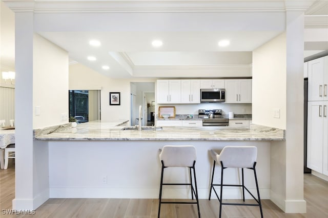 kitchen with stainless steel appliances, a peninsula, a sink, and white cabinetry