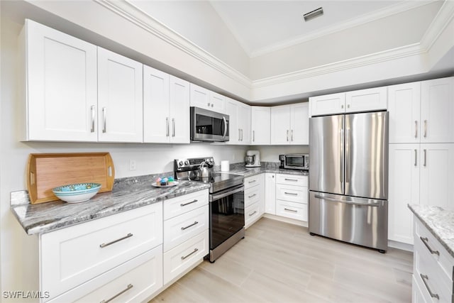 kitchen with stainless steel appliances, white cabinetry, vaulted ceiling, and light stone counters