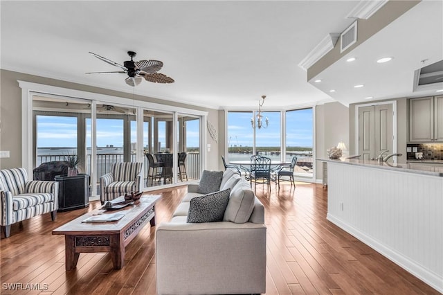 living room featuring crown molding, ceiling fan with notable chandelier, hardwood / wood-style flooring, and a water view