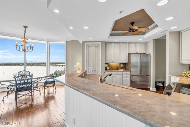 kitchen featuring stainless steel refrigerator, decorative light fixtures, light stone counters, a raised ceiling, and a water view