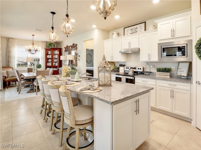 kitchen featuring stainless steel appliances, a center island with sink, white cabinets, and decorative light fixtures