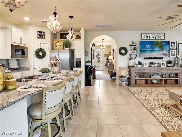 kitchen featuring a breakfast bar, light stone counters, hanging light fixtures, white cabinets, and appliances with stainless steel finishes