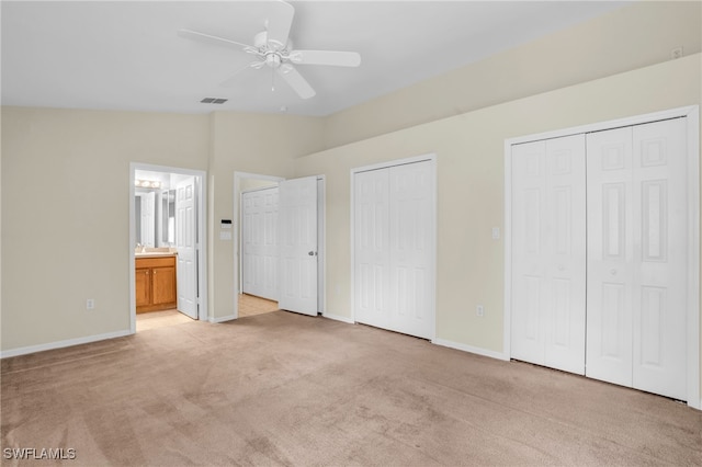 unfurnished bedroom with two closets, ensuite bathroom, vaulted ceiling, light carpet, and ceiling fan