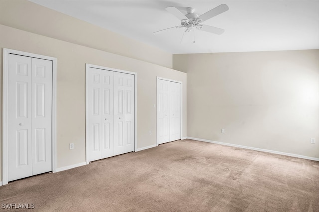 unfurnished bedroom featuring carpet, vaulted ceiling, ceiling fan, and multiple closets