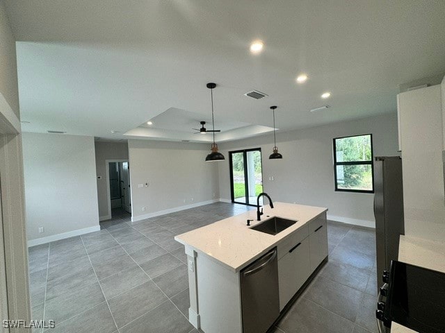 kitchen with a raised ceiling, a center island with sink, stainless steel dishwasher, sink, and white cabinets