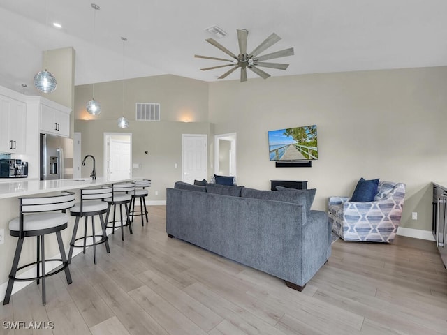 living room featuring light wood-type flooring, high vaulted ceiling, ceiling fan, and sink