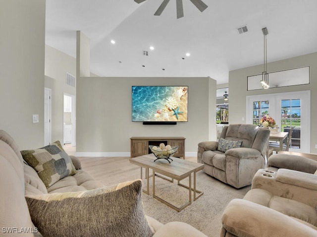 living room with ceiling fan, light wood-type flooring, a towering ceiling, and french doors