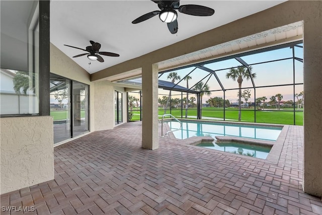 pool at dusk with a lawn, ceiling fan, a lanai, and an in ground hot tub