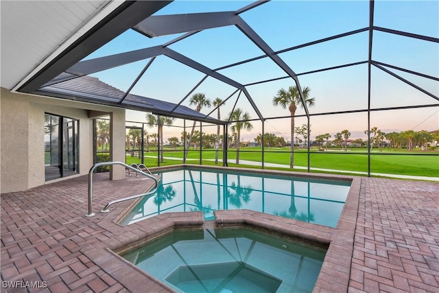 pool at dusk with an in ground hot tub, a patio, glass enclosure, and a lawn