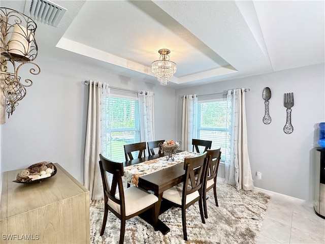 dining area with visible vents, a raised ceiling, a wealth of natural light, and a chandelier