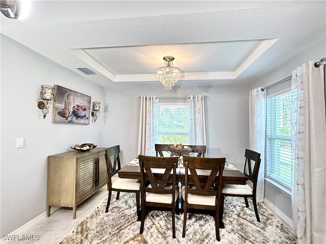 dining area with a tray ceiling, plenty of natural light, and an inviting chandelier