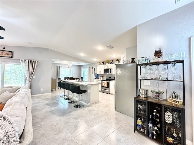 kitchen with a breakfast bar area, stainless steel appliances, visible vents, open floor plan, and vaulted ceiling