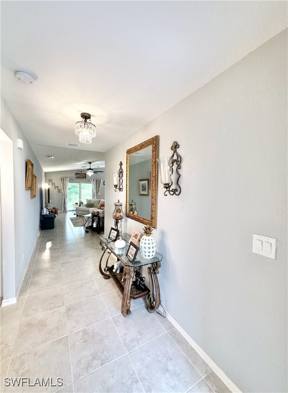 corridor featuring a chandelier, light tile patterned flooring, and baseboards