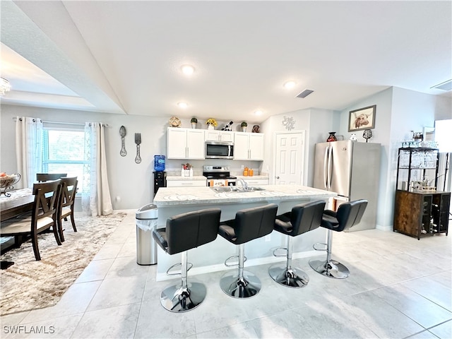 kitchen featuring appliances with stainless steel finishes, white cabinets, visible vents, and a kitchen bar