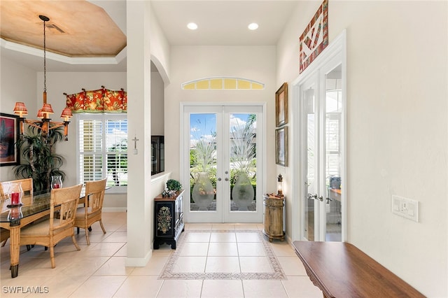 tiled entryway with french doors, an inviting chandelier, a tray ceiling, and plenty of natural light