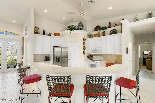 kitchen with ceiling fan, white appliances, backsplash, white cabinetry, and a kitchen breakfast bar