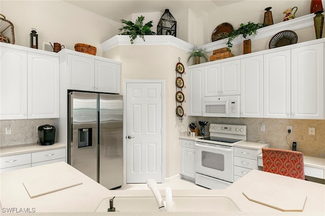 kitchen with backsplash, white appliances, and white cabinetry