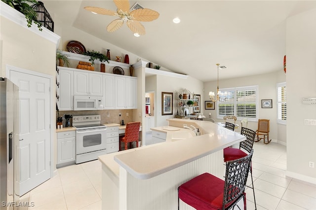 kitchen with white cabinets, lofted ceiling, hanging light fixtures, white appliances, and ceiling fan with notable chandelier