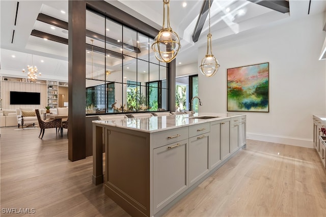 kitchen with pendant lighting, an island with sink, light wood-type flooring, sink, and light stone countertops