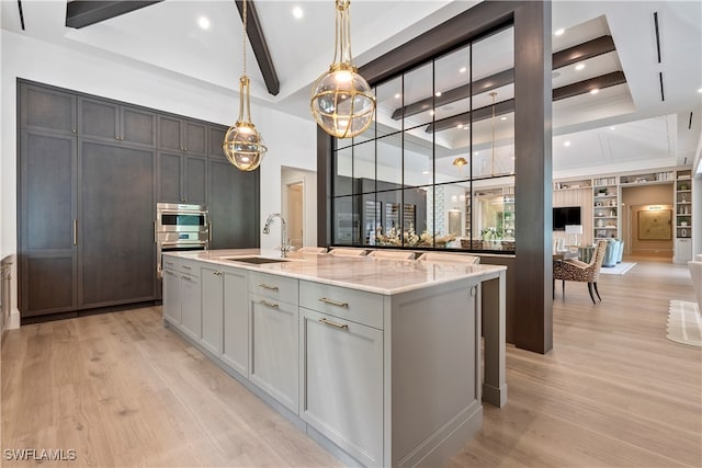 kitchen with light wood-type flooring, light stone counters, hanging light fixtures, gray cabinetry, and a center island with sink