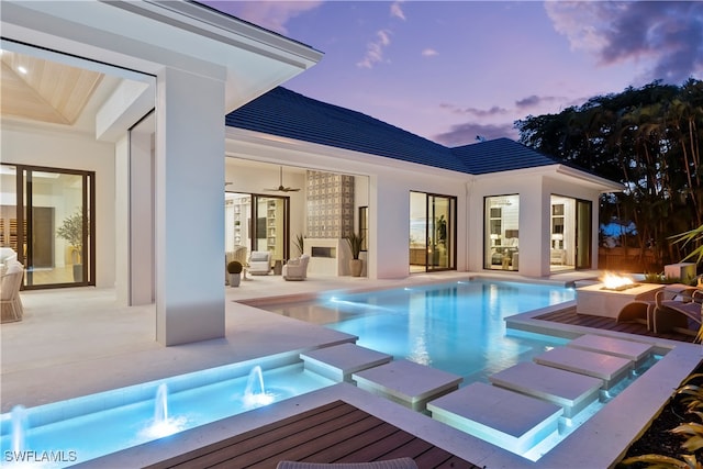 pool at dusk featuring pool water feature, ceiling fan, an in ground hot tub, and a patio area