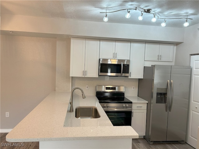 kitchen with light hardwood / wood-style flooring, appliances with stainless steel finishes, white cabinetry, sink, and kitchen peninsula