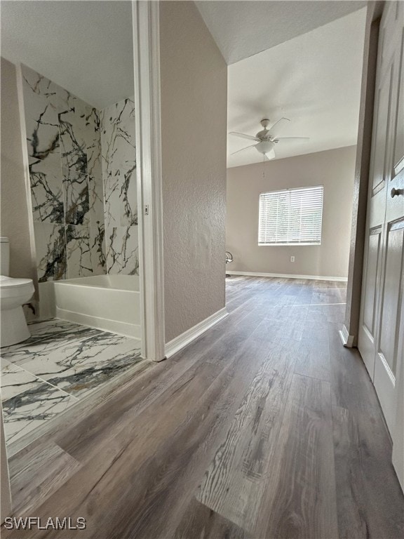 interior space featuring hardwood / wood-style floors, ceiling fan, toilet, and shower / bath combination